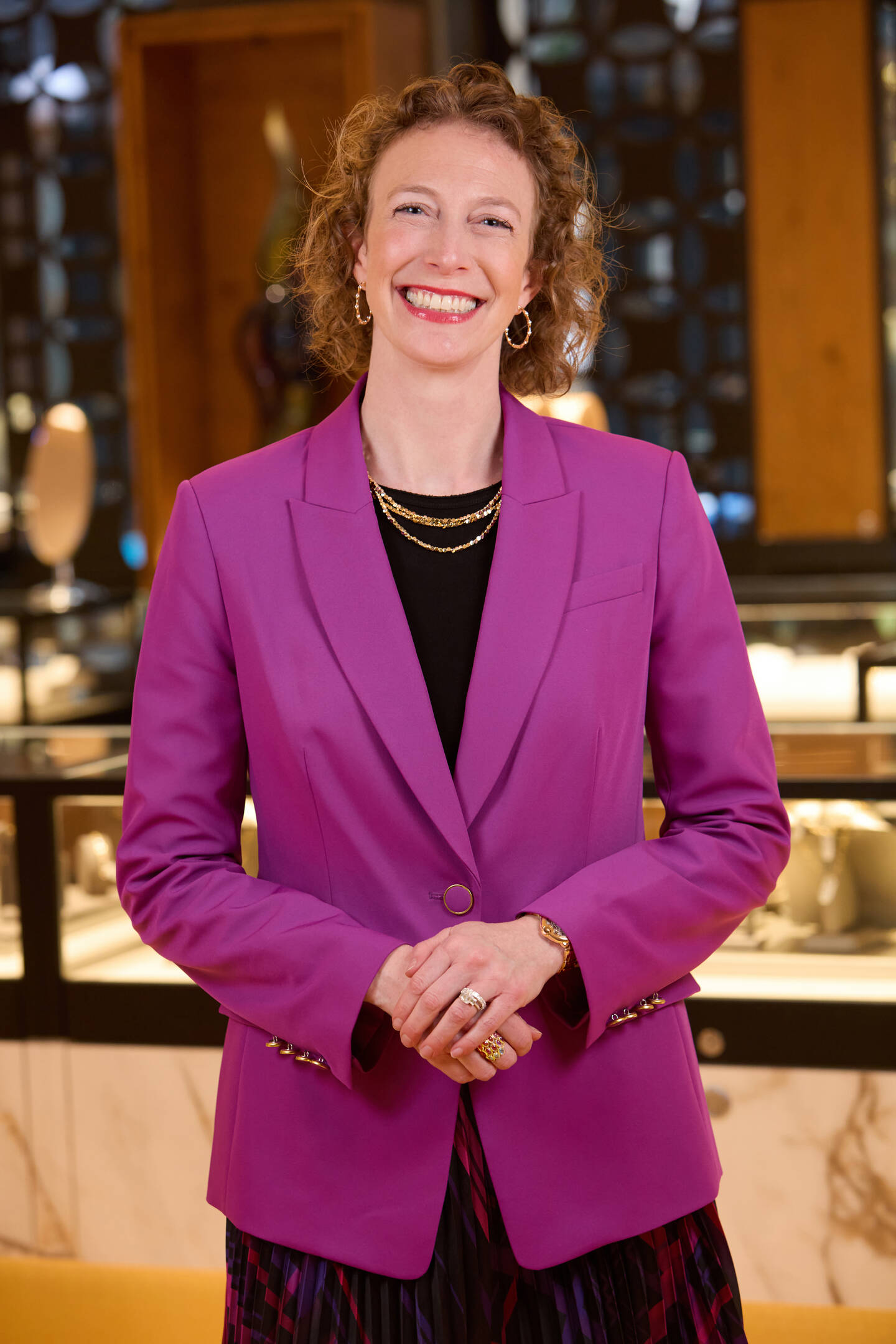 Lisa Bridge smiling in a pink jacket wearing gold earrings and necklaces. 